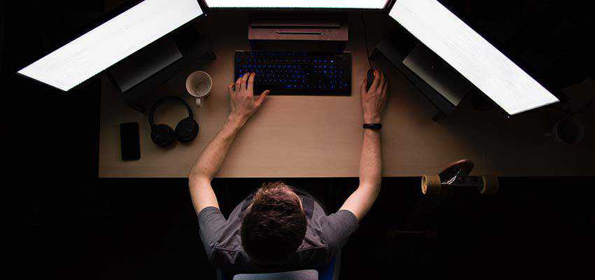 Man in front of three computer monitors.